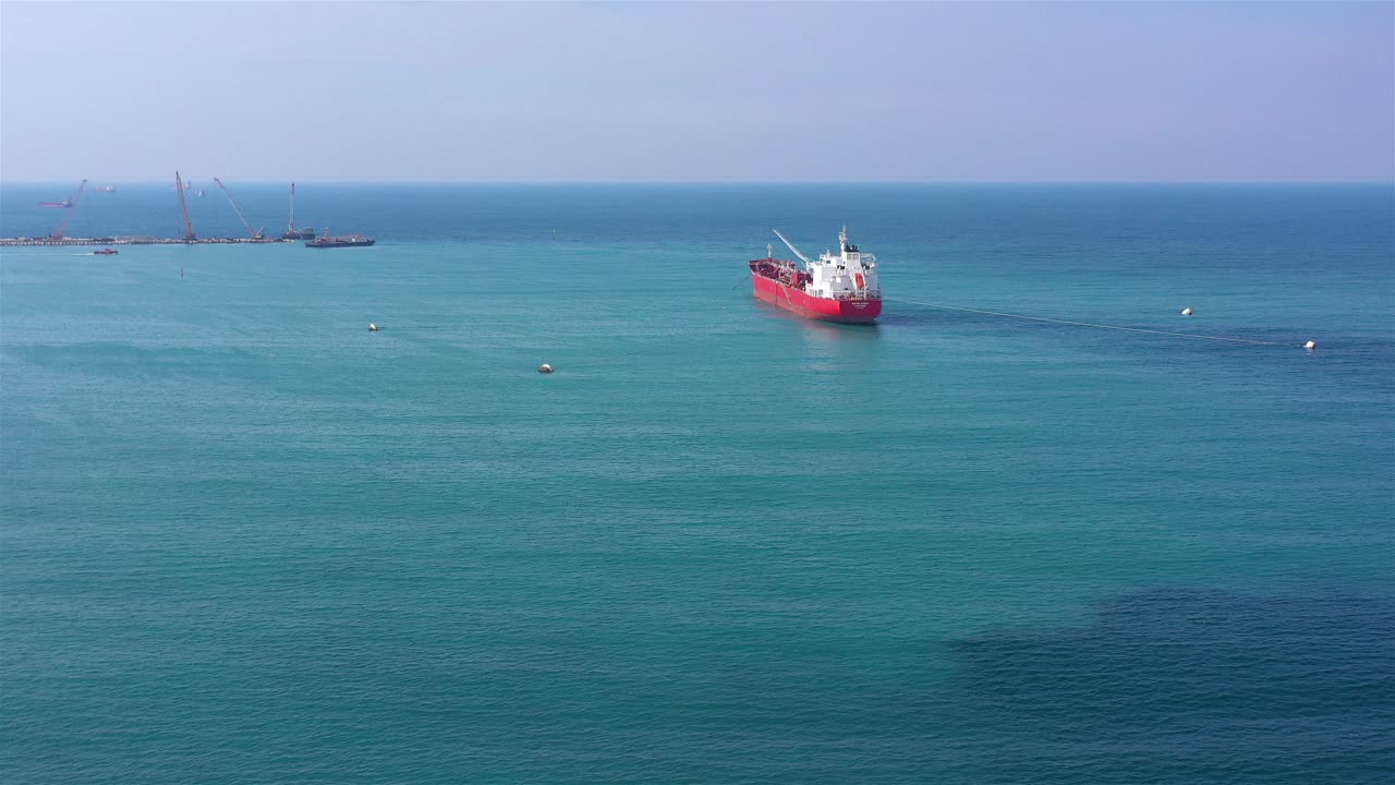 Red Cargo Ship in Calm Blue Sea with Distant Port Activity