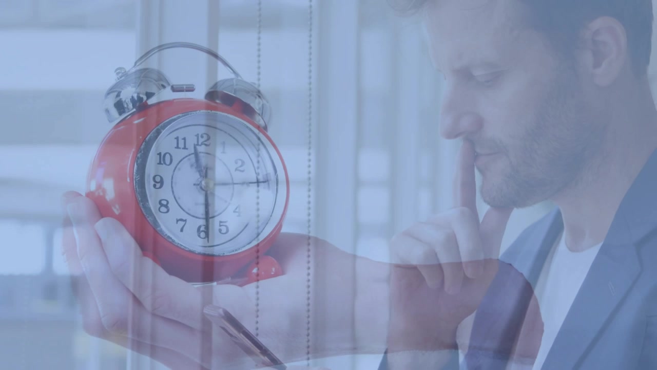 Mature man holding red alarm clock and touching chin, then tapping touchscreen, checking schedule