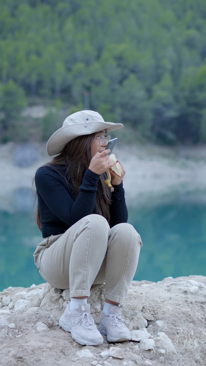 Woman eating a banana and using phone by a lake