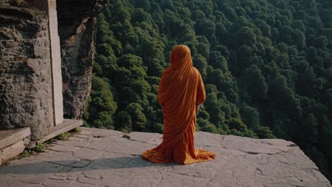 meditative buddhist monk wearing bright orange robes sitting in peaceful pose atop mountain temple, panoramic forest landscape spread below serene spiritual setting