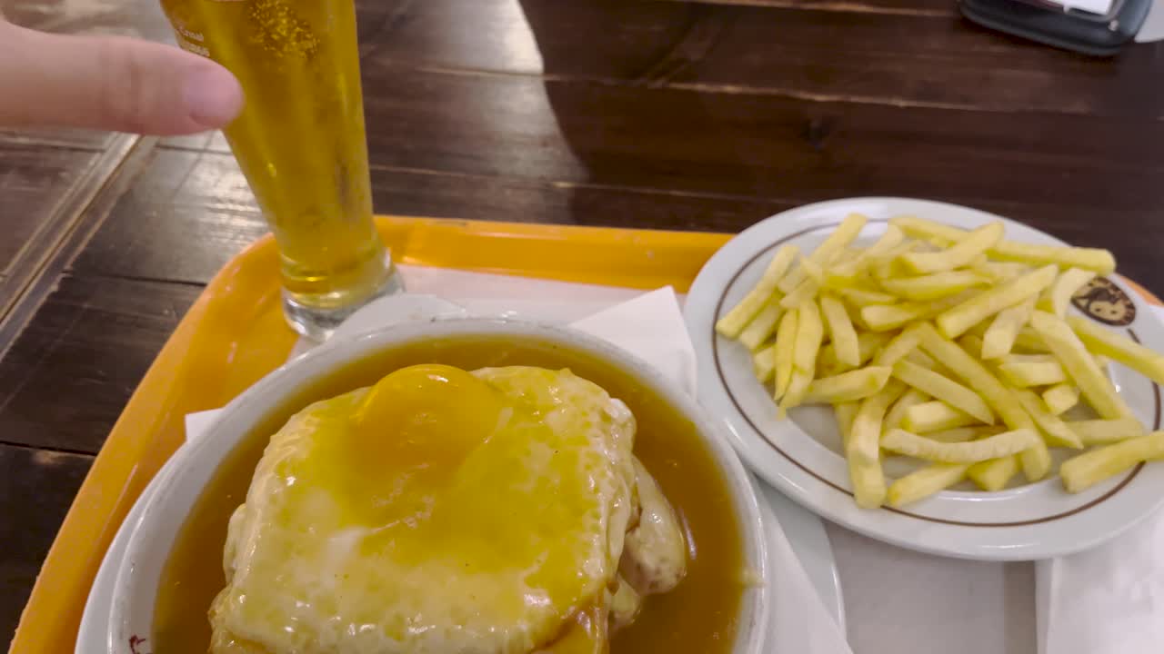 francesinha con huevo y salsa típica portuguesa, acompañado de papas fritas y una cerveza fría
