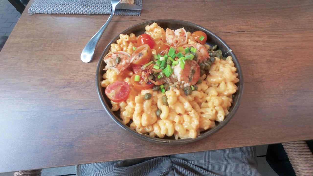 Deliziosi maccheroni al formaggio guarniti con pomodorini, cipollotti ed erbe aromatiche, serviti in una ciotola rustica su un tavolo di legno di un ristorante, scattati con luce naturale e una composizione invitante