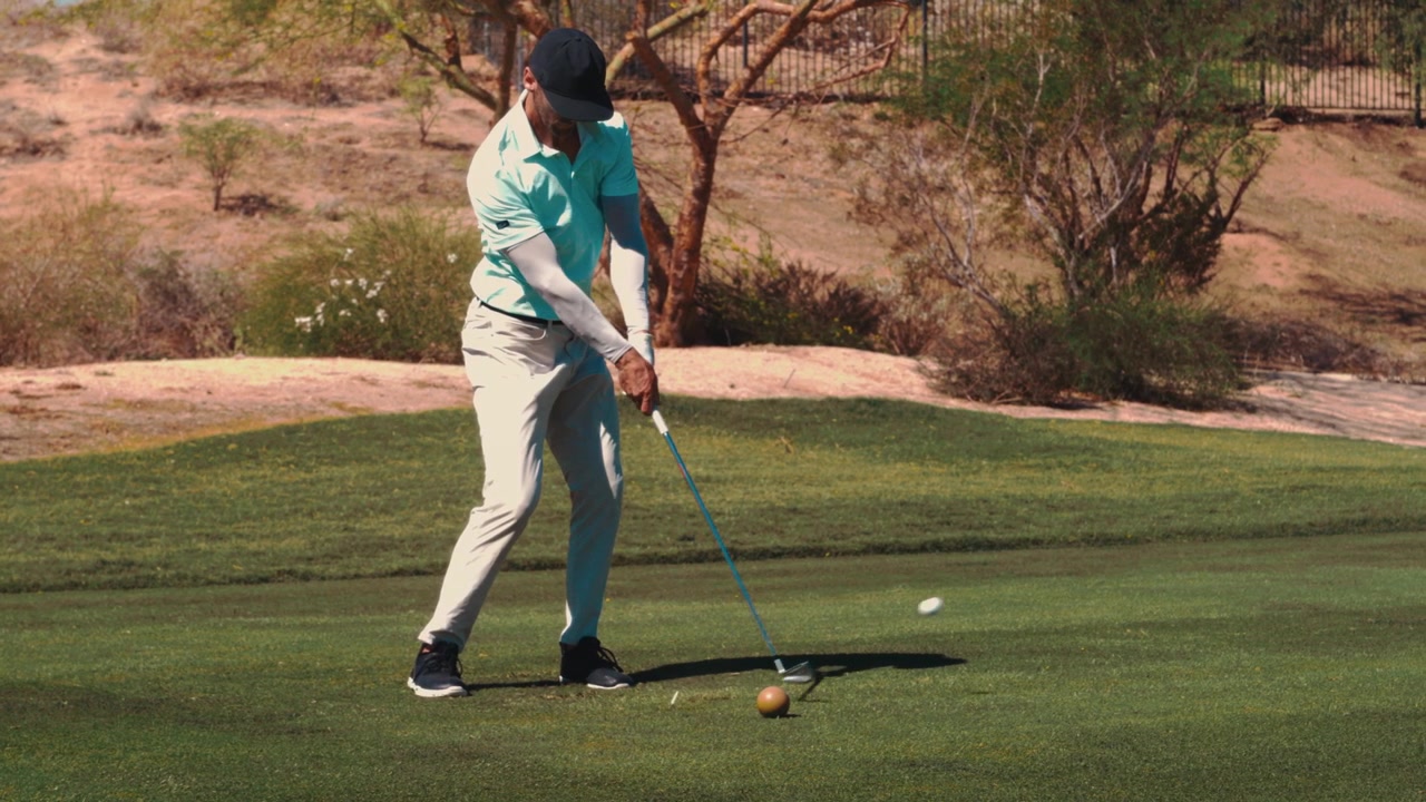 Golfista colpisce la palla dal tee su un par 3 in slow motion estremo, campo da golf nel deserto in una calda e soleggiata giornata estiva