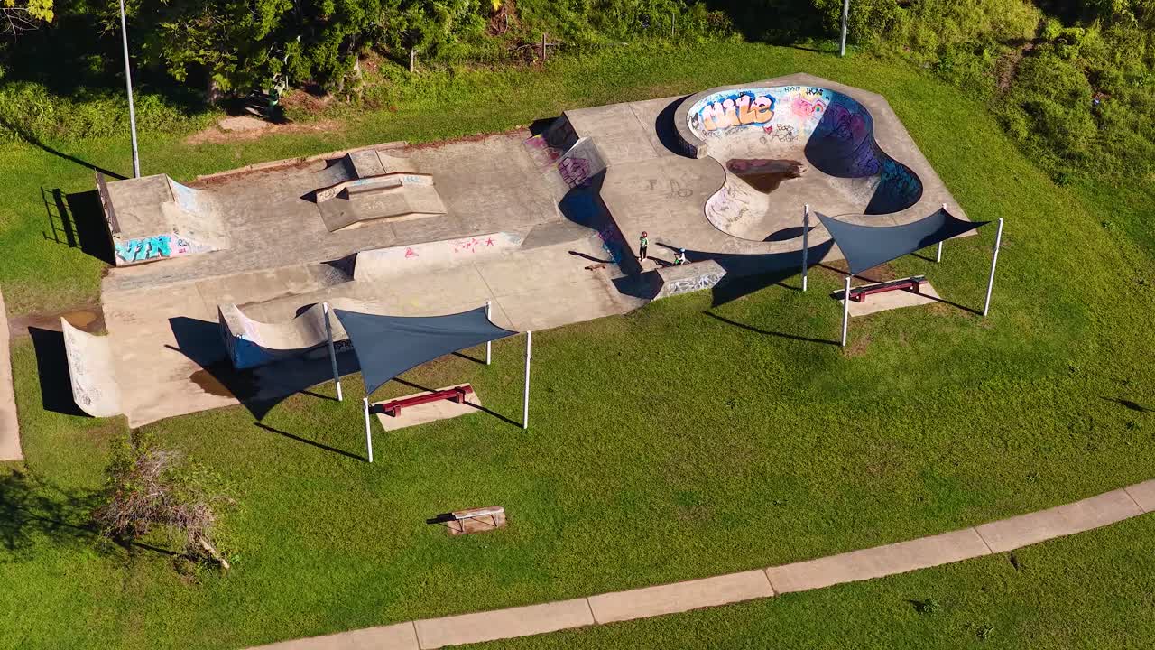 Korkealta kuvattu drone-kuva vangitsee hiljaisen betonisen skeittipuiston, jota ympäröi rehevä vihreä ruoho.