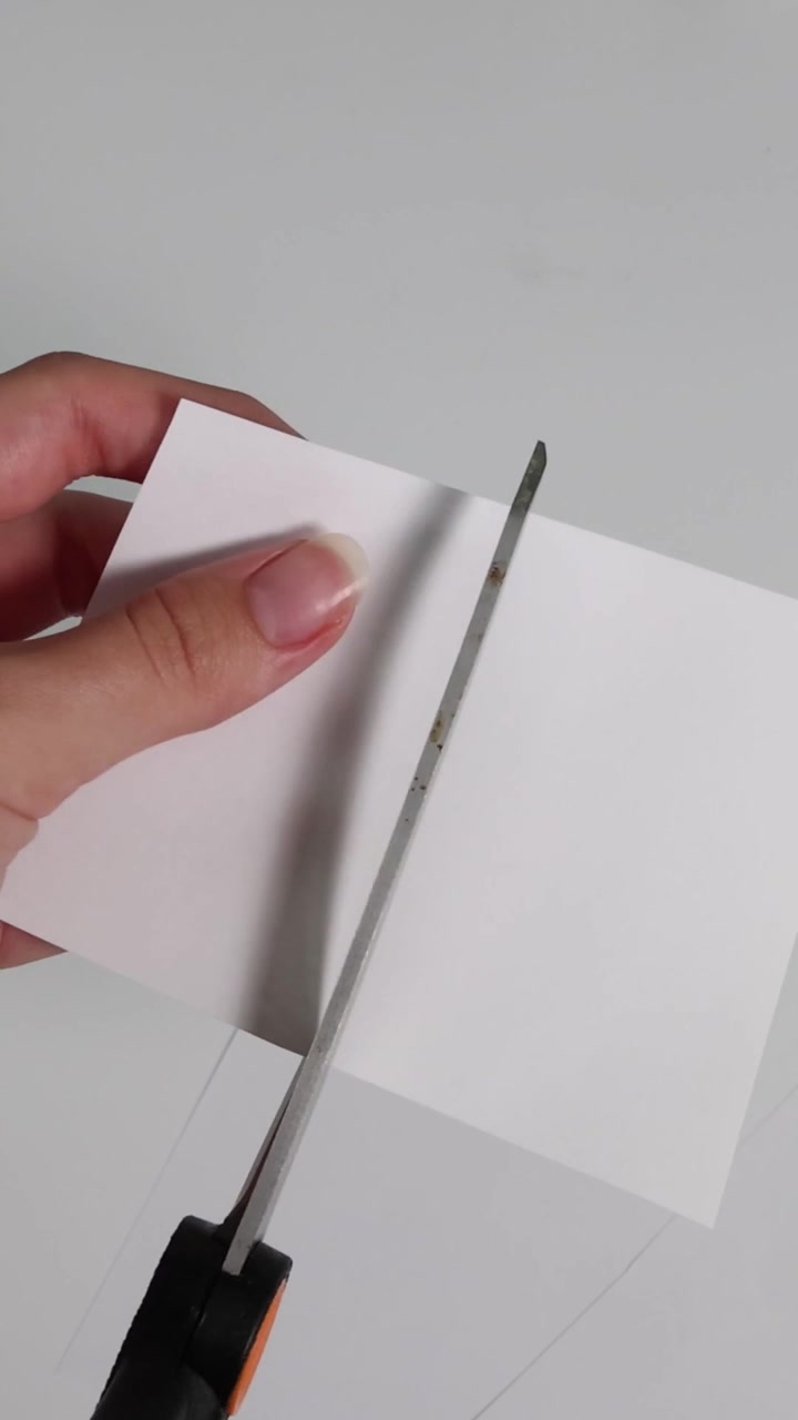 Un'inquadratura verticale dettagliata che mostra mani che usano le forbici per tagliare forme da carta bianca