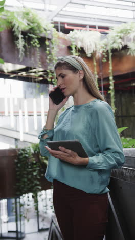 vertical video of caucasian female creative talking on smartphone at casual office, in slow motion