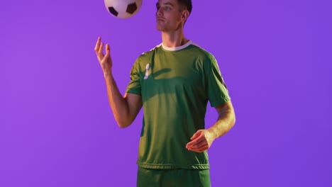 caucasian male soccer player with football over neon pink lighting