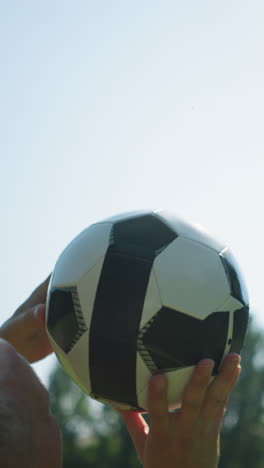 close-up of a middle-aged man skillfully rotating a soccer ball in the air and catches it back, with blurred trees in the background and a clear sky
