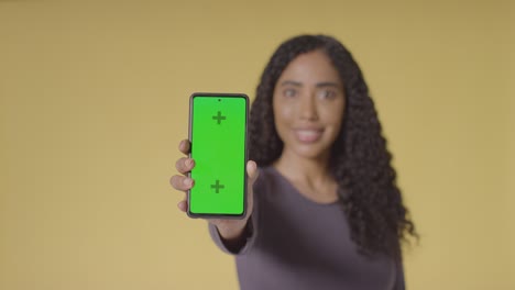 studio portrait of smiling woman holding up mobile phone with green screen