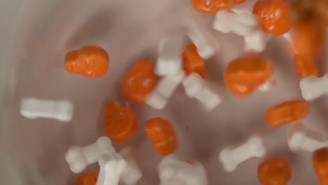 Nahaufnahme-Von-Orangefarbenen-Totenköpfen-Und-Bonbons-In-Form-Von-Bonbons,-Die-Langsam-Auf-Einen-Teller-Fallen