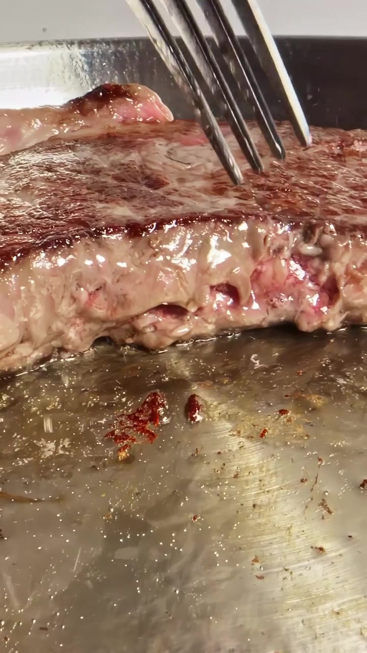 Saftig bøf steger på en varm metalplade, med boblende saft og brunende stegeskorpe under skarpt køkkenlys, hvilket skaber et mundvandsløbende nærbillede.