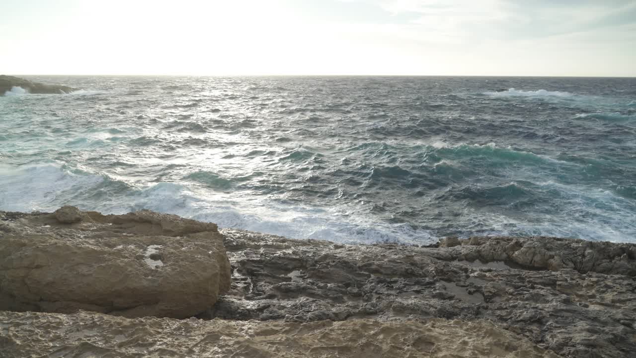 praia de calcário com ondas quebrando na costa da ilha de gozo durante dia de vento em dezembro