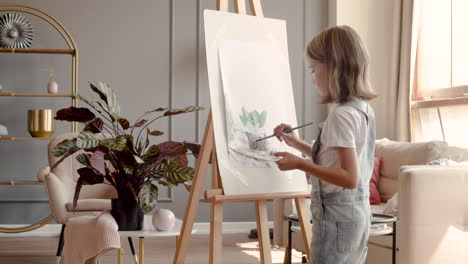 rear view of a blonde girl painting a plant with a brush on a lectern in the living room at home 3