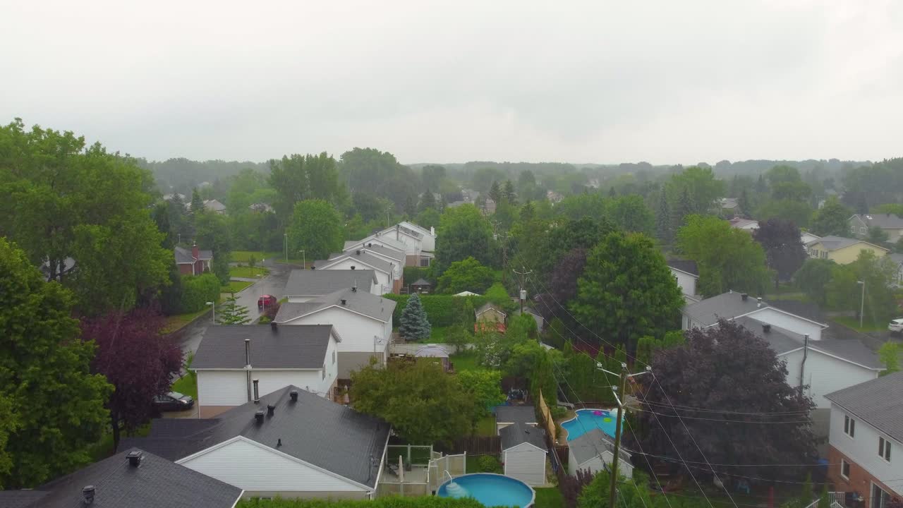 White houses with gray roof, surrounded lush trees under rainy sky filled with clouds in Montreal, Quebec, Canada, serene atmosphere.