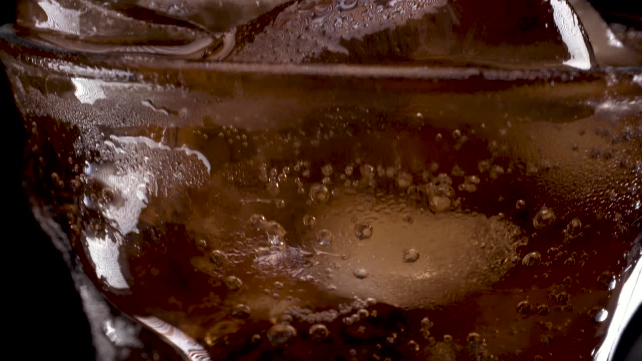 cola y hielo en vidrio, inclinando hacia arriba un primer plano macro de vidrio moderno con curvas 4k uhd 2160p sobre fondo negro
