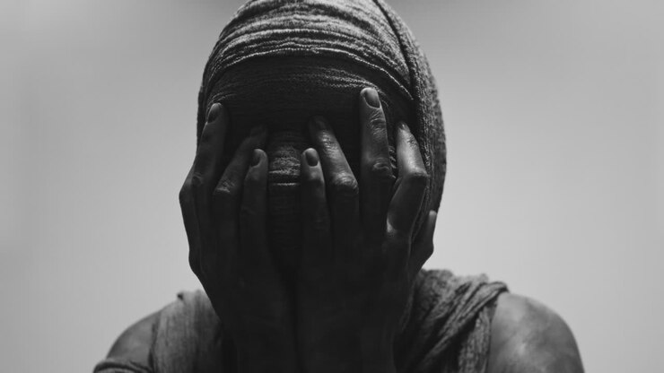 Una donna mummificata su uno sfondo luminoso tiene le mani sul viso in una posa potente e piena di disperazione