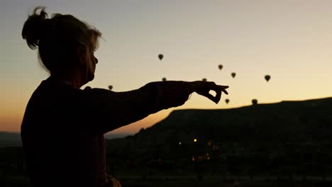 Silueta-De-Mujer-Apunta-Hacia-El-Cielo-Temprano-En-La-Mañana-Amanecer-Globos-De-Aire-Caliente