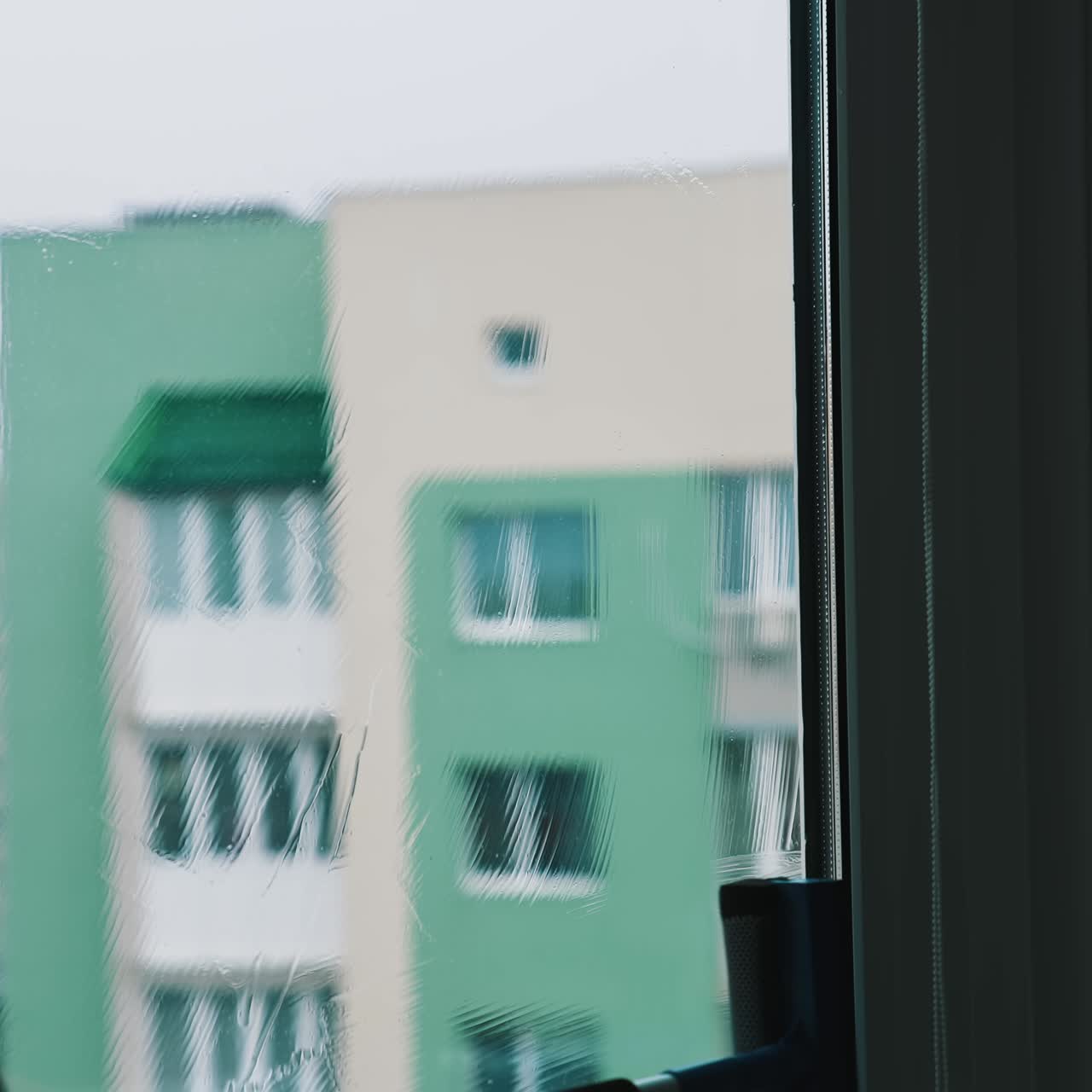 Process of washing window at home in the city. Silhouette of a man cleaning glass window with a brush and special liquid in flat on high building background