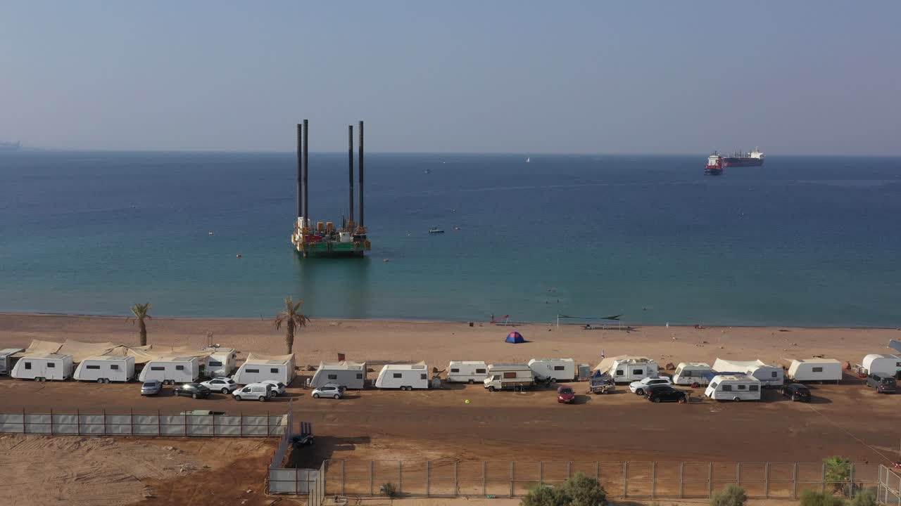 una plataforma autoelevadora o una plataforma móvil de unidad autoelevadora en un área costa afuera frente al camping público de la playa hadatiyim en un día soleado, ciudad de eilat, israel - carretilla aérea a la derecha