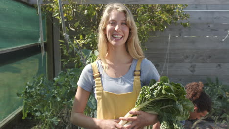 Portrait-of-happy-diverse-couple-working-in-garden-and-holding-fresh-vegetables,-slow-motion