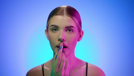una joven rubia caucásica se pinta los labios mirando a la cámara, un primer plano en un estudio de belleza