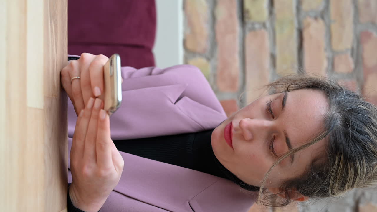 Close up of a woman in a pink blazer typing on her phone in a restaurant. Vertical