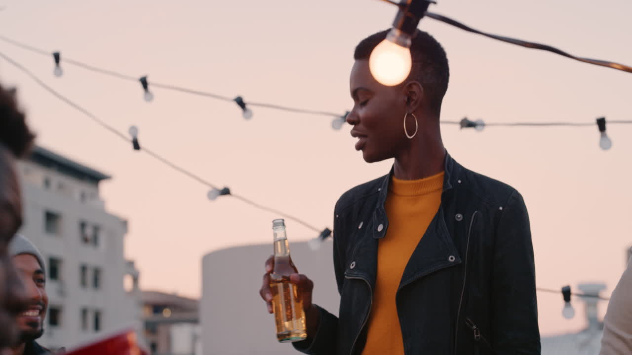 beautiful african american woman enjoying rooftop party celebration chatting to friends socializing drinking alcohol sharing celebration at sunset
