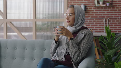 beautiful muslim business woman drinking coffee using smartphone browsing social media messages texting sharing successful career ideas wearing hijab headscarf in modern office workplace