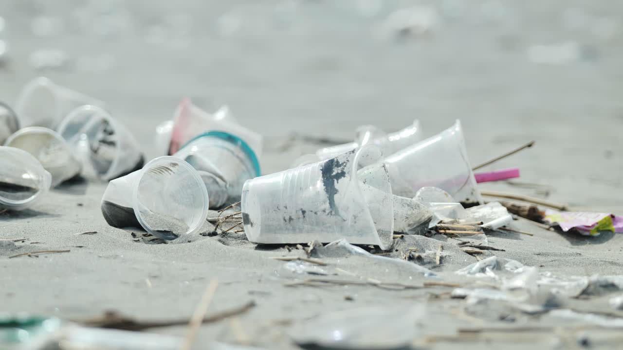 Primo piano di rifiuti di plastica sparsi sulla sabbia della spiaggia di Lingayen sotto la luce soffusa del giorno.