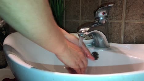 Closeup-of-thorough-hand-washing-with-white-soap-over-oval-washbasin-and-single-handle-faucet-in-bathroom-with-brown-limestone-tiles-in-4k