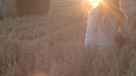 woman enjoying sunset in hay field with hay bale