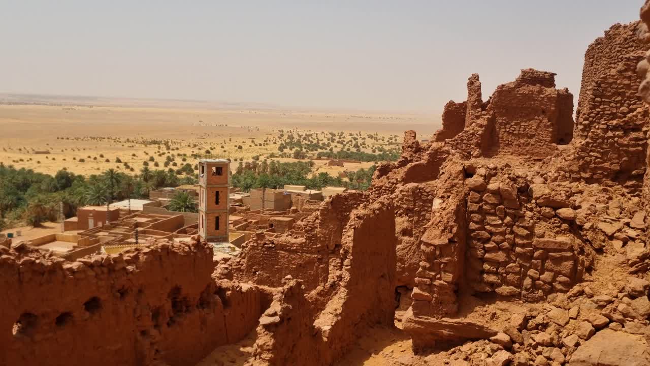 Shot over ancient castle ruins (Ksar) and a nearby traditional village near Timimoun, Algeria, under the blazing sun of a scorching Saharan desert day