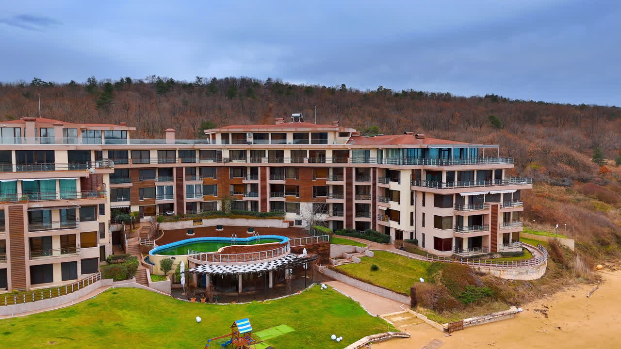 Letecký pohled na komplex přímořského letoviska s bazénem. Pohled shora na moderní hotelovou architekturu s bazénem a zeleným trávníkem poblíž pláže