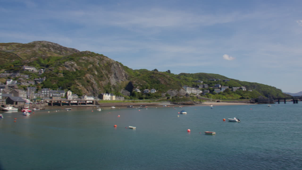 Panning wide shot right to left of the town of Barmouth with its Harbour and rail bridge on the Mawddach estuary with small boat