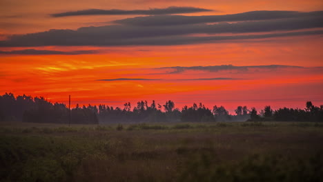 Static-shot-sunrise-through-the-clouds-over-a-fog-covered-green-field-in-timelapse