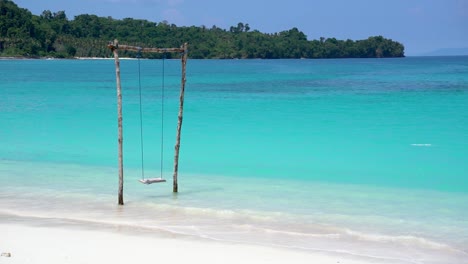 4k video of a wooden swing on a tropical beach in indonesia. crystal clear blue ocean waves crashing against the white sand beach in the banggai islands, sulawesi indonesia