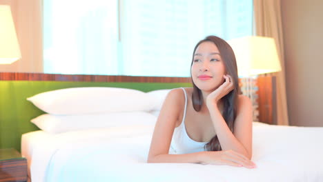 an asian woman comfortably lying on a bed in her room and changing her sight from one side to another, slow motion, face close-up