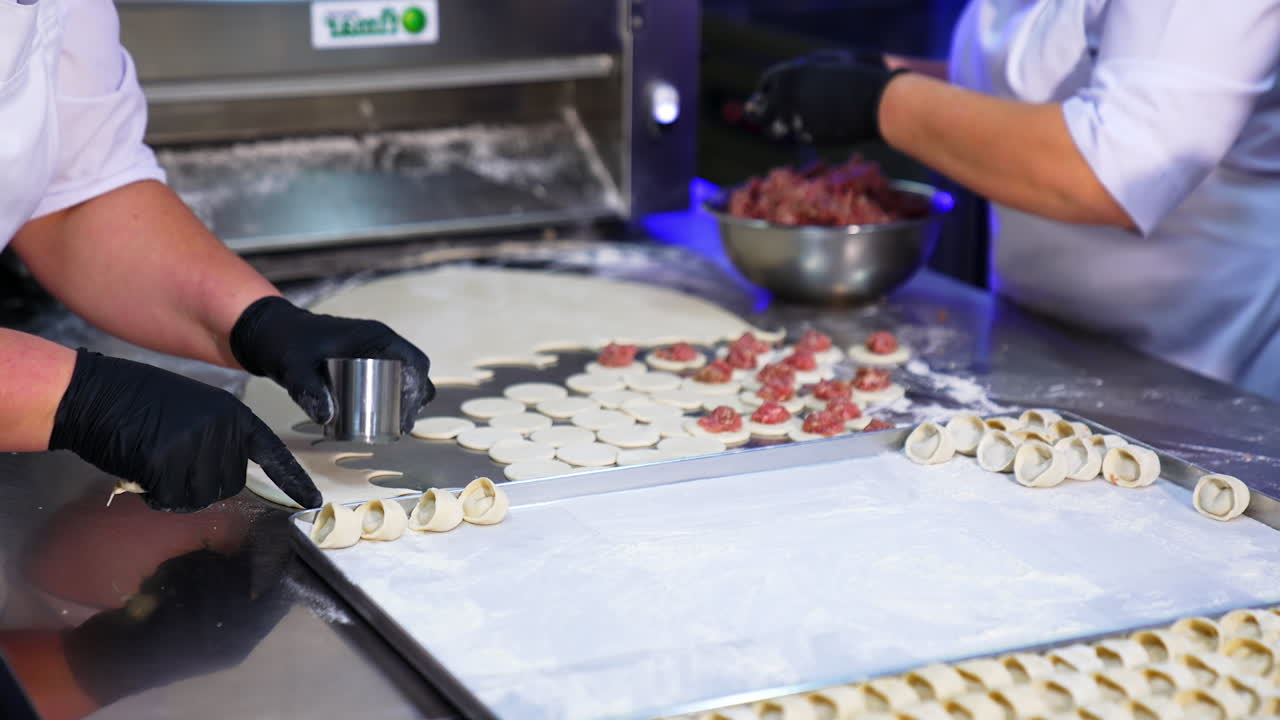 The process of manufacturing semi-cooked dishes in the restaurant. Cooks in black latex gloves produce handmade meat ravioli. Close up.