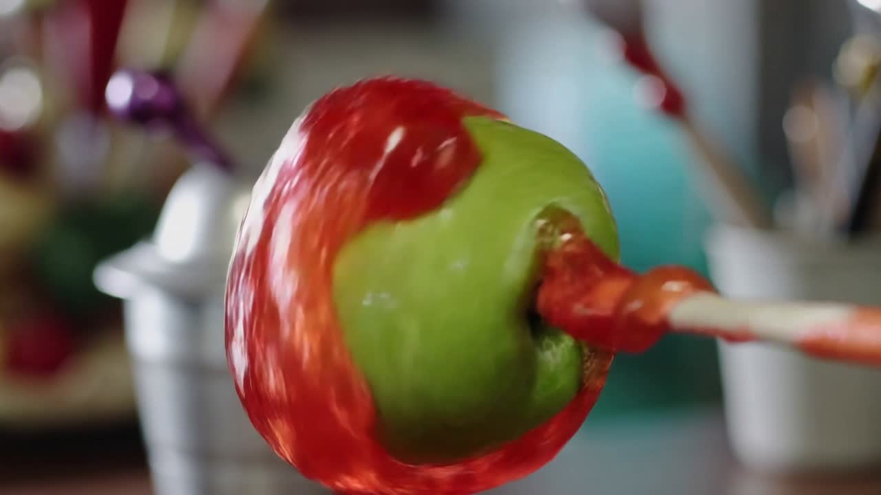 Rotating green apple on wooden stick at kitchen counter spreading glossy red glaze to coat