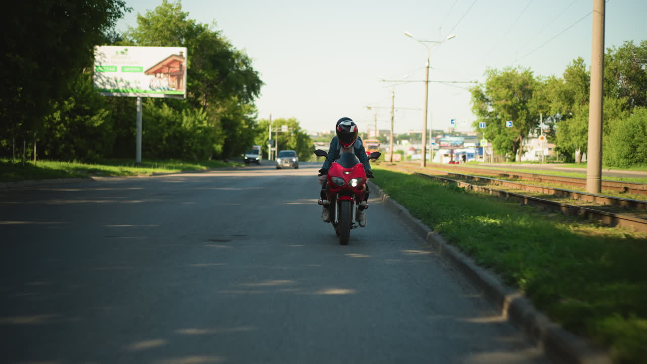dos damas montan una bicicleta eléctrica con cascos, viajando cerca de las vías del ferrocarril con postes eléctricos y señales en el fondo