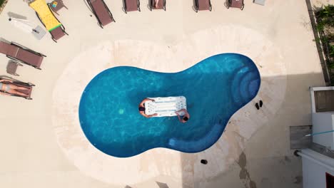 drone descending towards two friends playing beer-pong on inflatable mat in the swimming pool