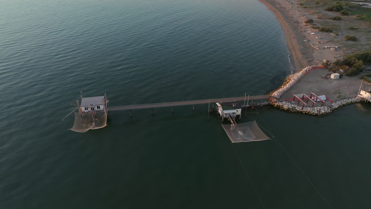 vista aérea en cámara lenta de cabañas de pesca a orillas del estuario al atardecer, máquina de pesca italiana, llamada "trabucco", lido di dante, ravenna cerca del valle de comacchio