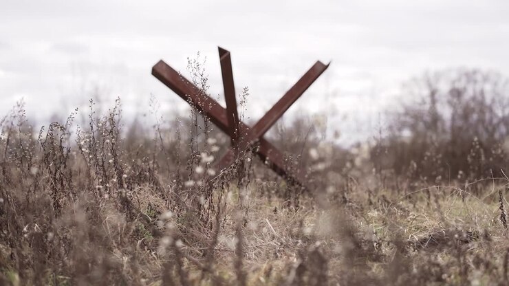 Rusty old anti-tank barrier in the meadow against the sky