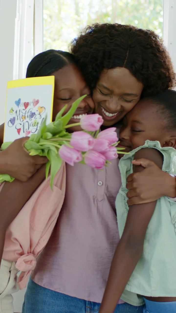 Vídeo vertical: Mãe entregando tulipas e cartão, adolescente com blusa amarrada abraçando a família na cozinha, com espaço para texto