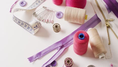 Video-of-tape-measure,-safety-pins,-reels-of-thread-and-zips-on-white-background