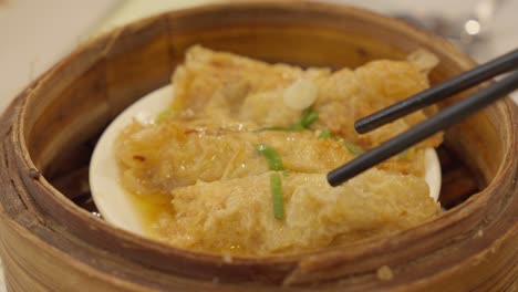 close up of dim sum dish and chopsticks picking up steamed tofu skin rolls on dipping sauce