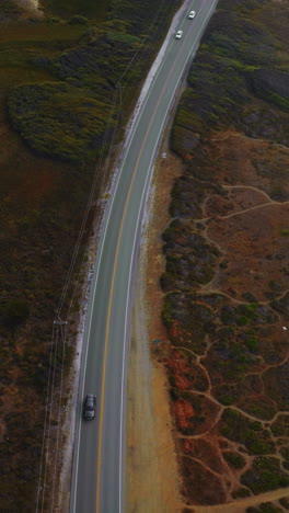 motorway going through the dry rocky landscape. drone descending over the highway with cars quickly moving by. vertical video