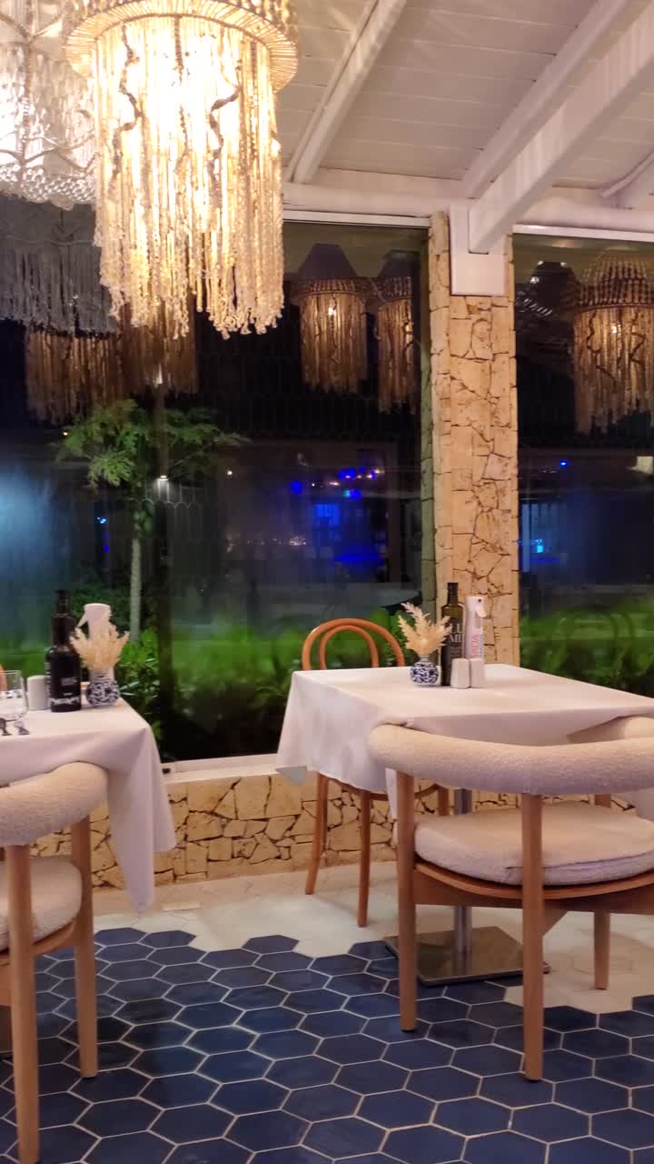 Elegant restaurant interior at night, with set tables, unique lighting, and view of raining outside
