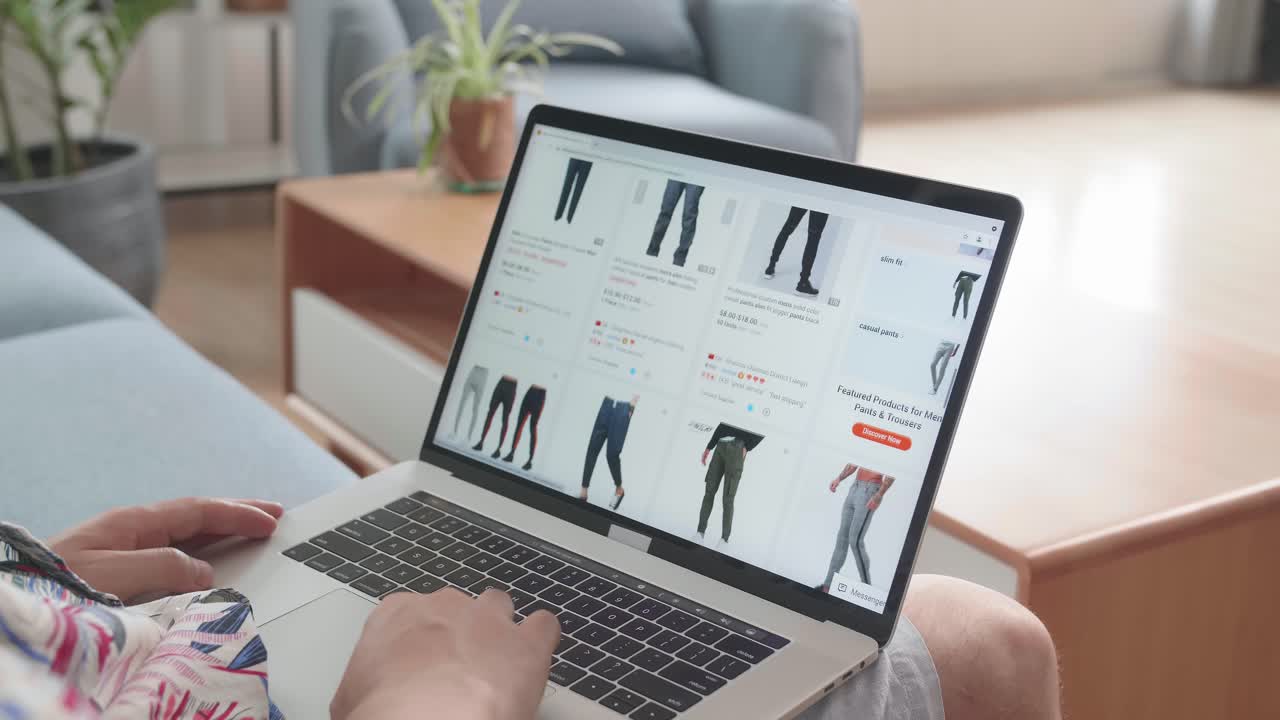 Asian Man Sitting On Couch And Using Laptop Computer Buys In Internet Shop. Buy Fashion Clothes Directly On Laptop Computer