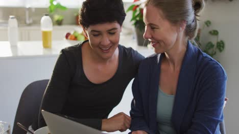 Mujer-Caucásica-Besando-A-Su-Esposa-Mientras-Realiza-Una-Videollamada-En-Una-Computadora-Portátil-En-Casa